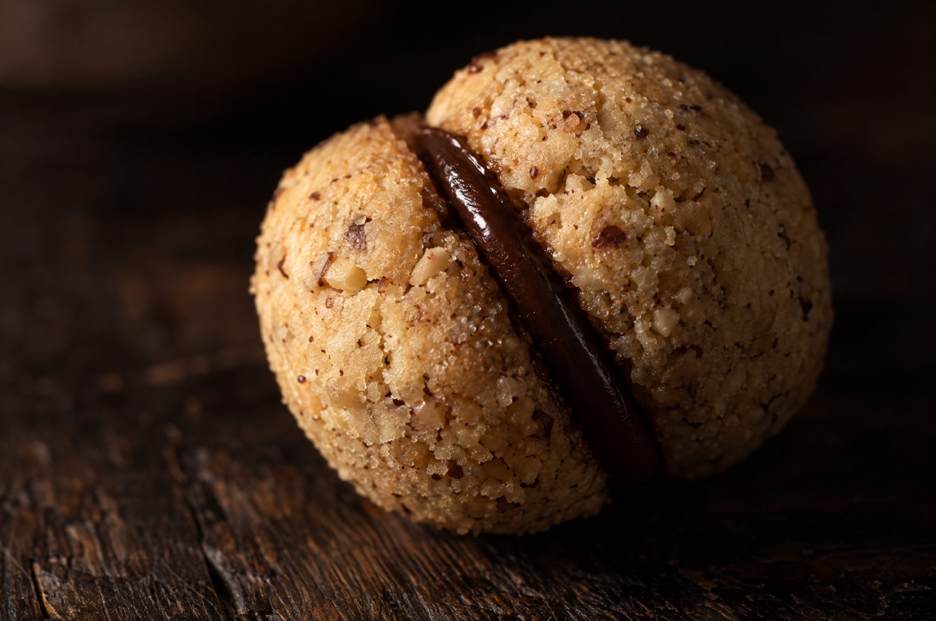 Close-up van baci di dama: twee ronde goudgele koepeltjes hazelnootdeeg met een laag glanzende pure chocolade ertussen