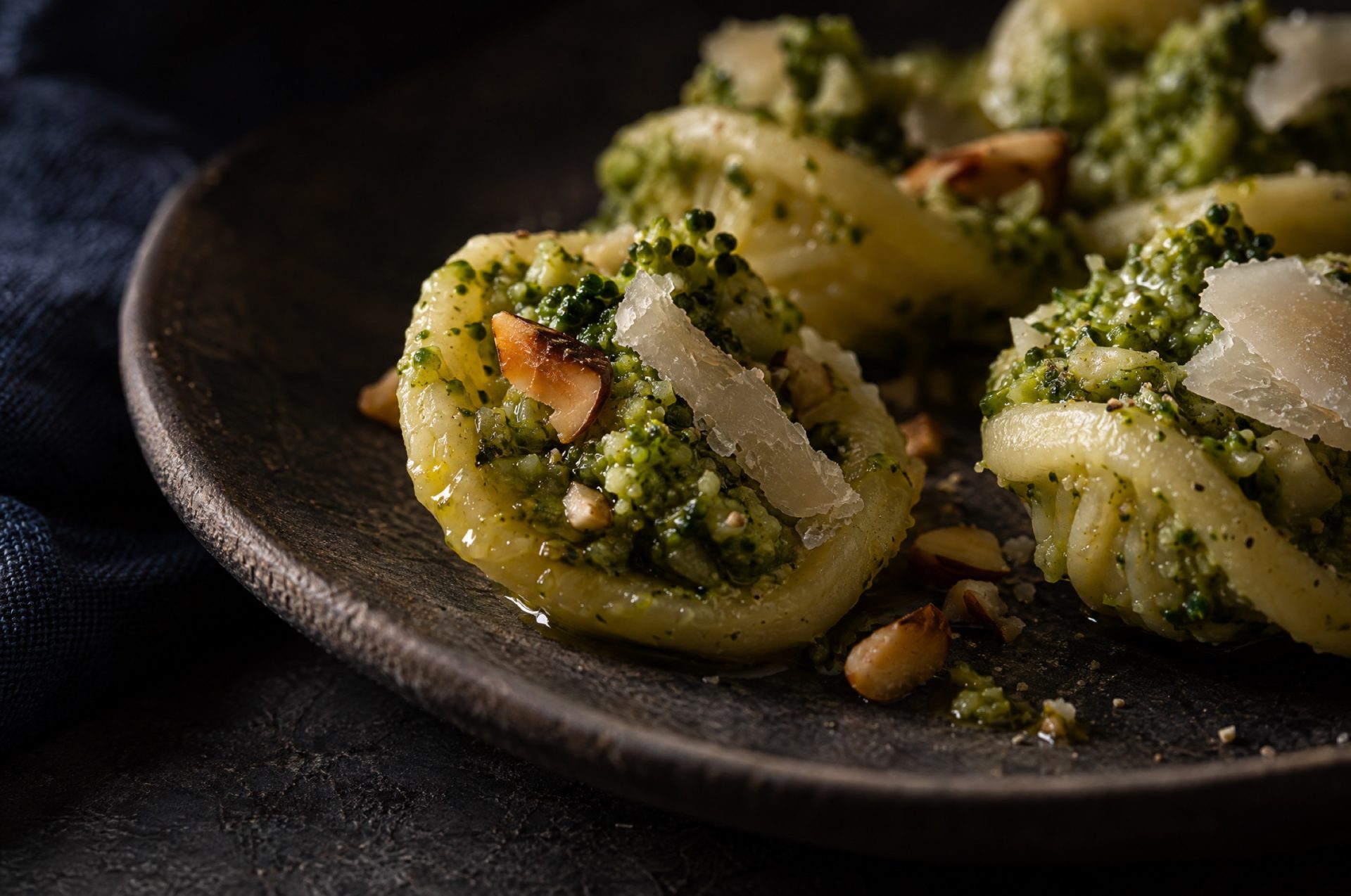 Close-up van broccolipesto op orecchiette: groene korrels, stukjes geroosterde amandel en een glans van olijfolie