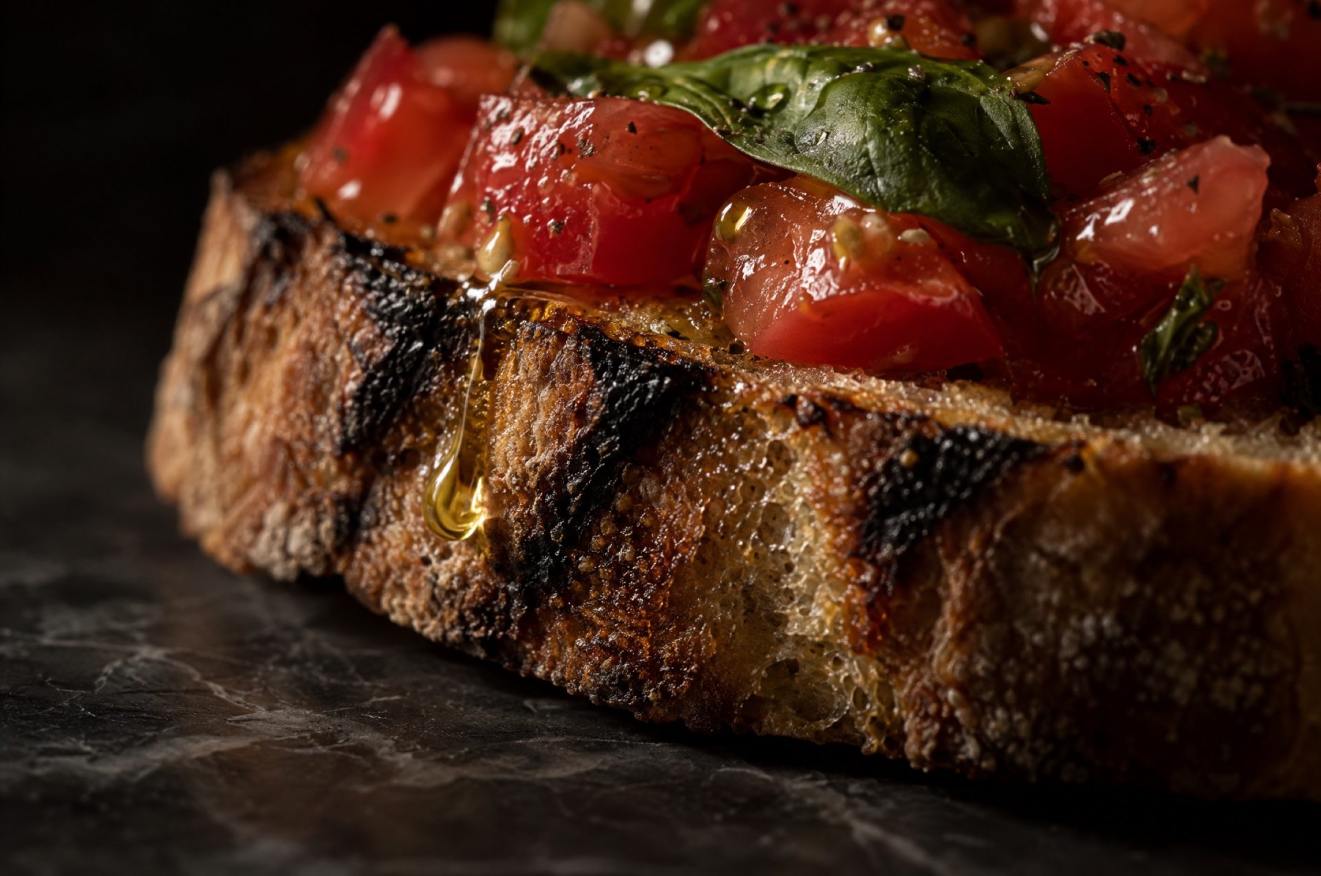 Close-up van bruschetta: goudbruine korst met donkere grillstrepen, glanzende tomatenblokjes en een druppel olijfolie