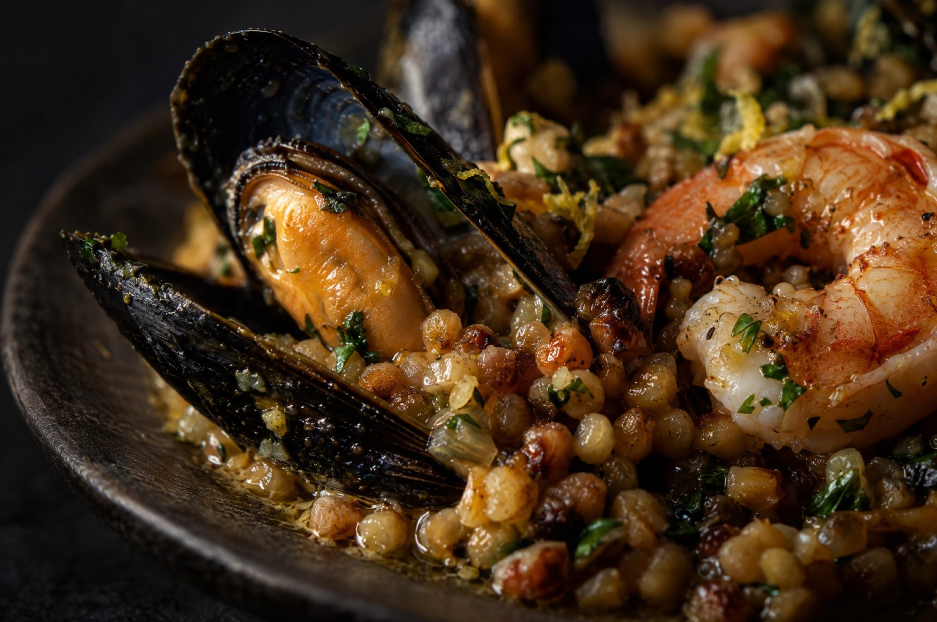 Close-up van fregola met zeevruchten: glanzende geroosterde korrels tussen een open mossel en een roze garnaal