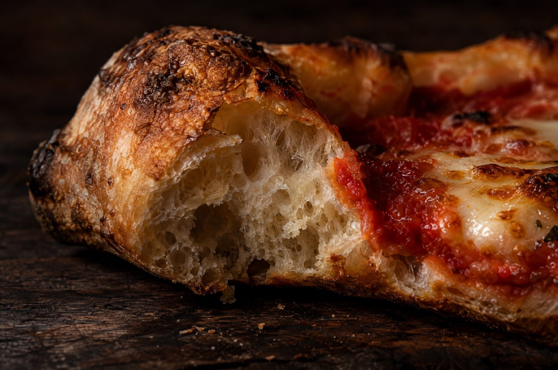 Close-up van gebakken glutenvrij pizzadeeg: een luchtige, gebarsten rand met kleine gaatjes in het kruim