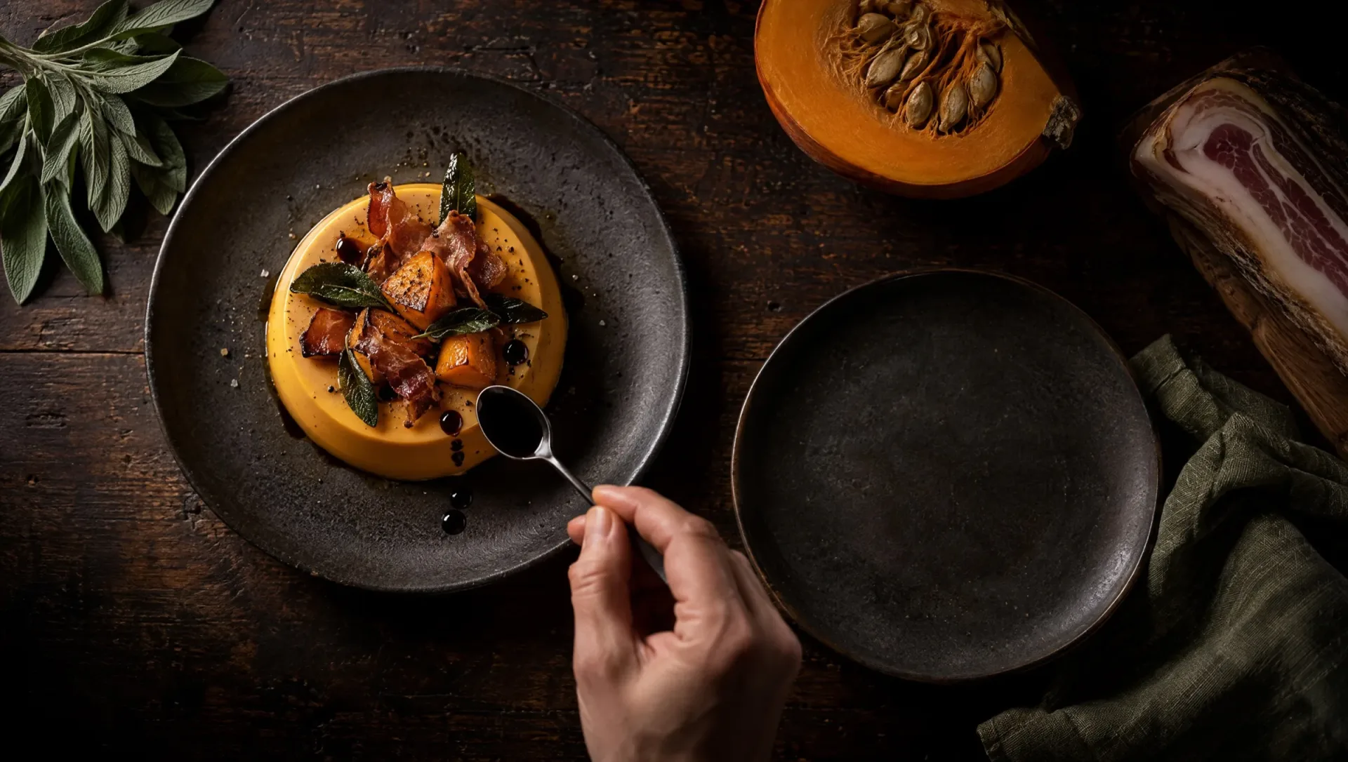 Hartige panna cotta van pompoen met pancetta en balsamico op een donkere tafel in Emilia, met rauwe pompoen en salie