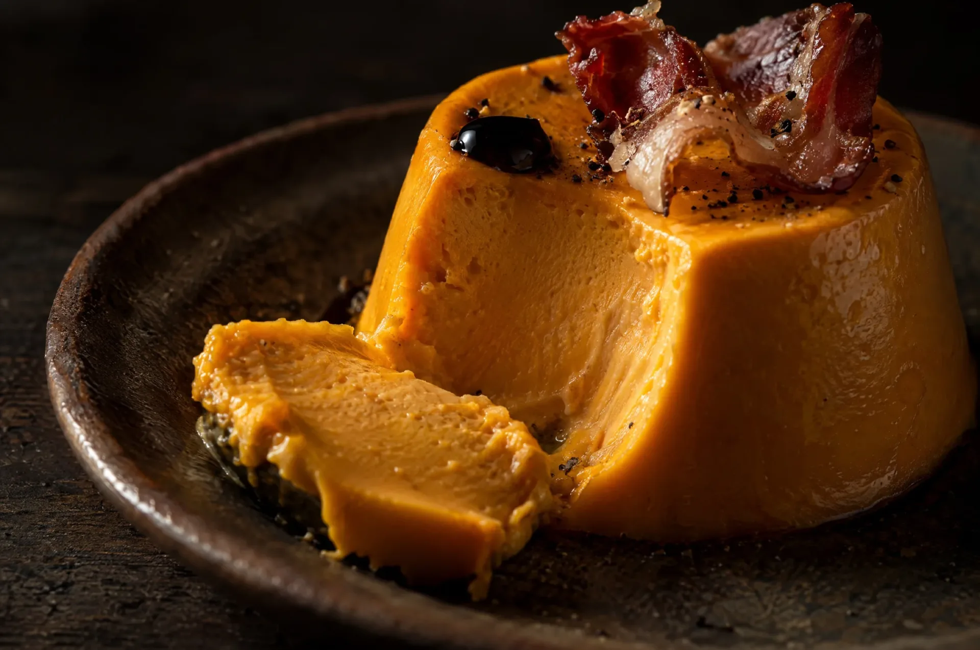 Close-up van hartige panna cotta van pompoen met een glad oranje snijvlak, krokante pancetta en een druppel balsamico