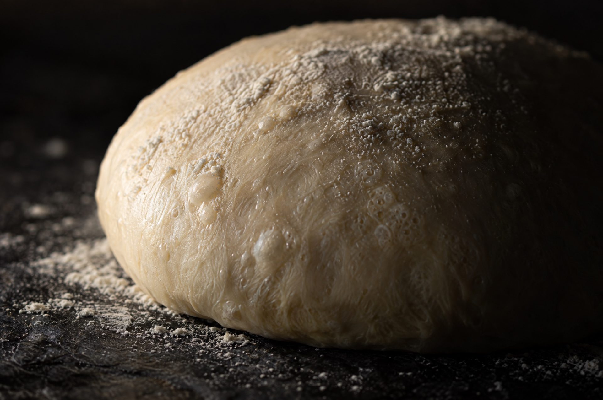 Close-up van een gerezen deegbal italiaans pizzadeeg met kleine luchtbellen onder het gladde, licht bestoven vel
