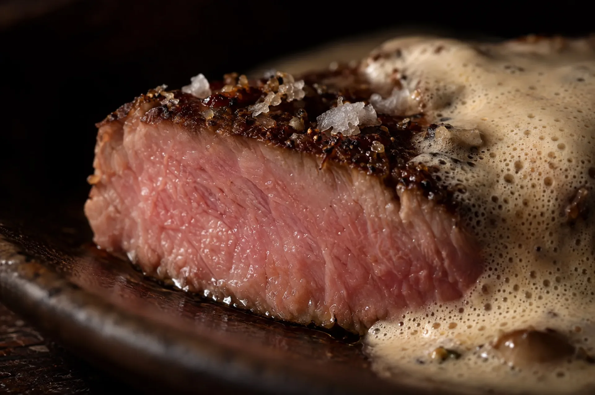 Closeup van kalfsfricandeau sous vide: bruine korst boven een egaal roze snijvlak met een laagje porcinischuim