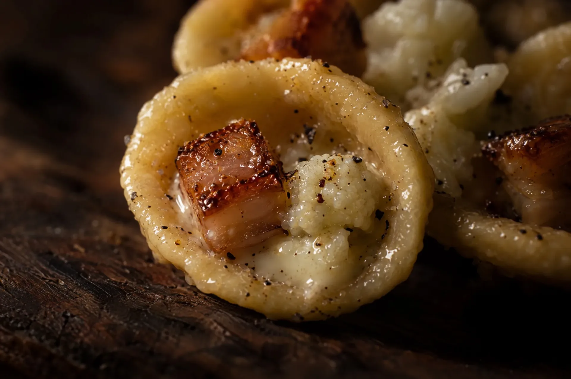 Close-up van orecchiette met bloemkool: een glanzend oortje met pecorino en een krokant blokje lardo erin