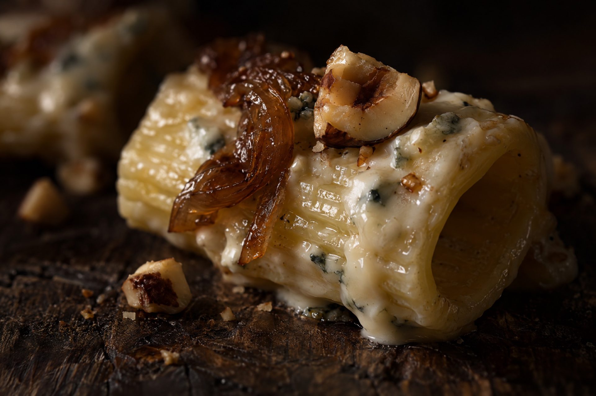 Close-up van pasta gorgonzola: glanzende gorgonzolacrème op een rigatone met gehakte hazelnoot en bruine ui