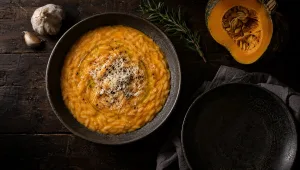 Pastina met pompoen in een diep bord op een donkere herfsttafel bij Mantova, met rauwe delica, rozemarijn en knoflook