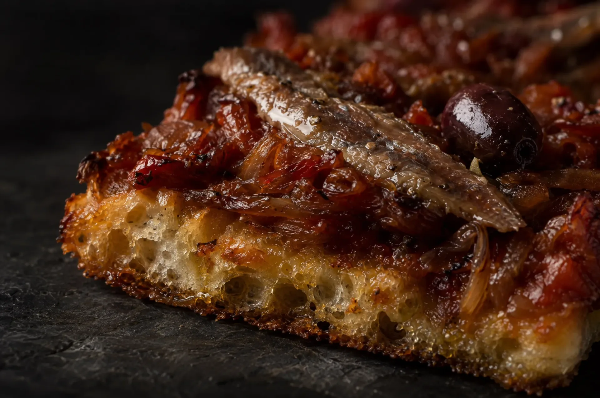 Detail van pissalandrea: de knapperige rand, gebakken in olie, met ansjovis en een Taggiasca-olijf op dikke tomatensaus
