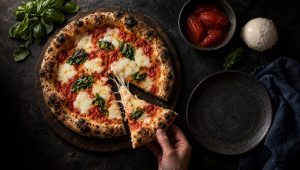 Pizza margherita op een donkere houten plank, met San Marzano-tomaten, mozzarella en verse basilicum ernaast