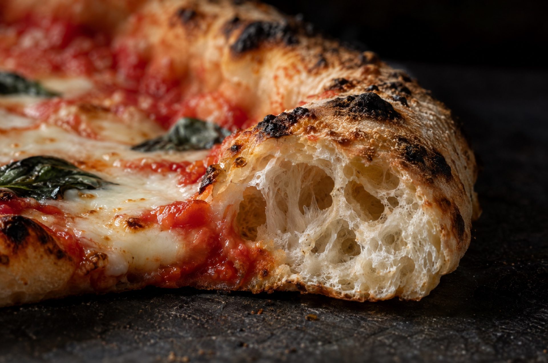 Close-up van de rand van een pizza margherita, met grote luchtbellen in de kruim en zwarte vlekjes op de korst