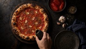 Pizza marinara op een donkere houten plank, met rauwe tomatensaus, plakjes knoflook, oregano en een glans van olijfolie