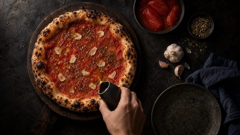 Pizza marinara op een donkere houten plank, met rauwe tomatensaus, plakjes knoflook, oregano en een glans van olijfolie