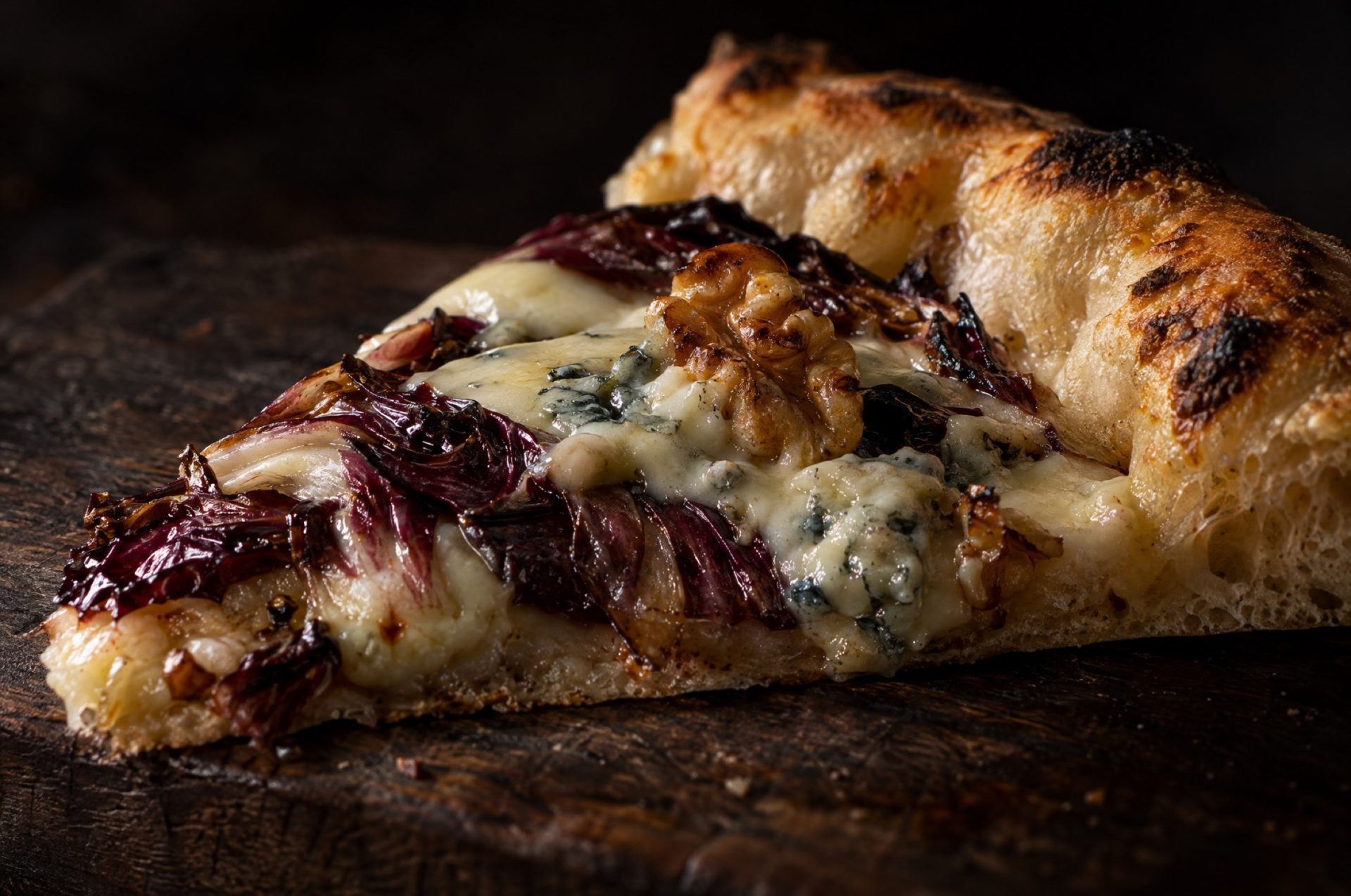 Close-up van pizza met gorgonzola: gesmolten kaas en walnoten op een donkerrode reep radicchio, met de rand erachter