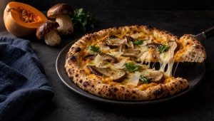 Pizza met pompoen en porcini op een donker bord, met flespompoen, verse porcini en peterselie ernaast