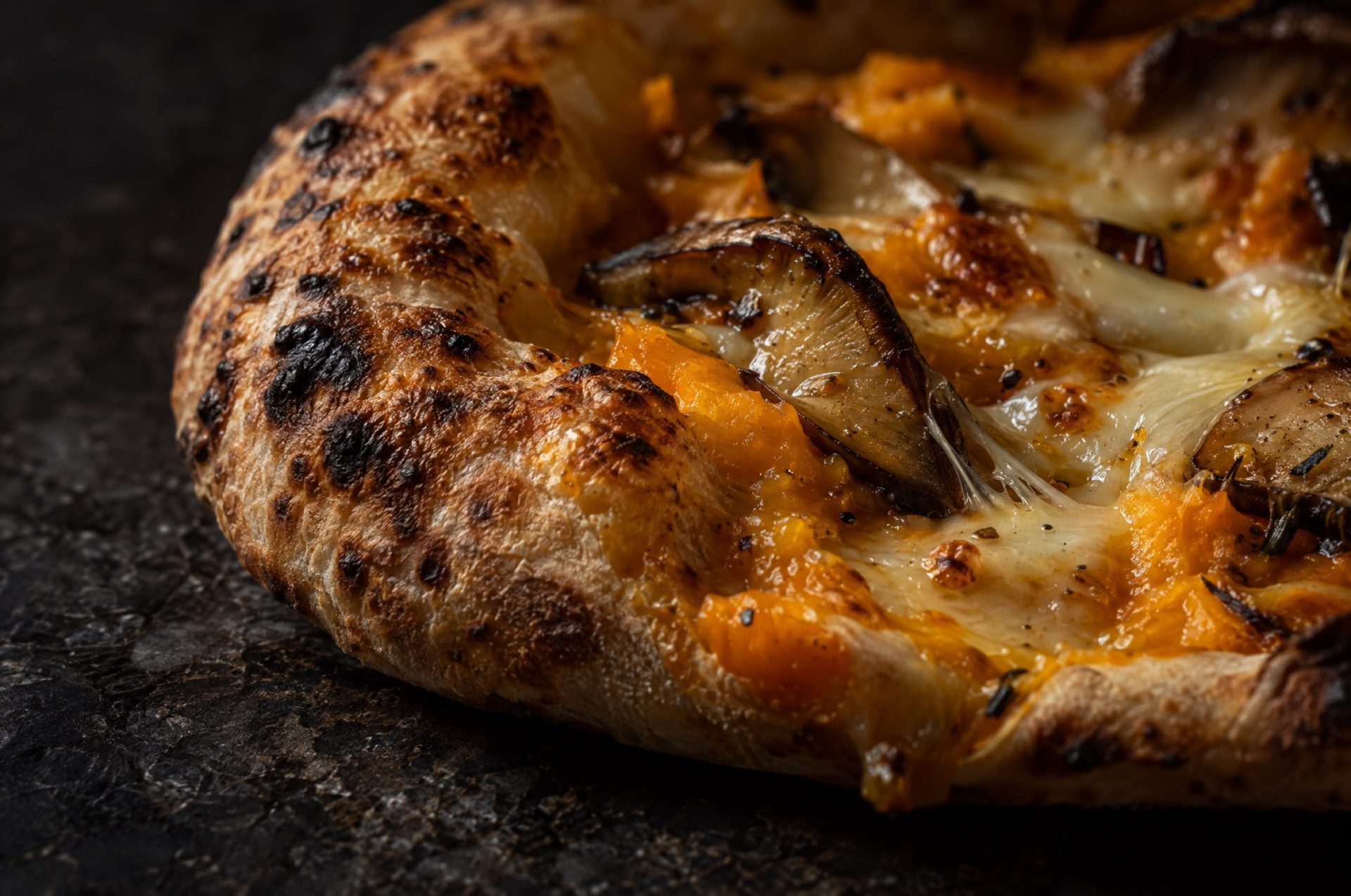 Close-up van de rand van pizza met pompoen en porcini, met luchtige blazen, donkere vlekjes en gesmolten provola