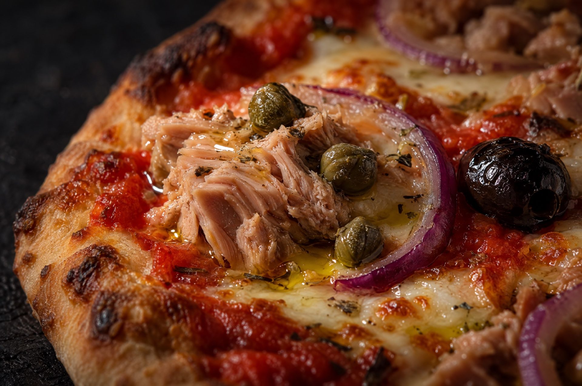 Close-up van pizza met tonijn: een stuk tonijn met kappertjes op gesmolten mozzarella en zachte rode ui