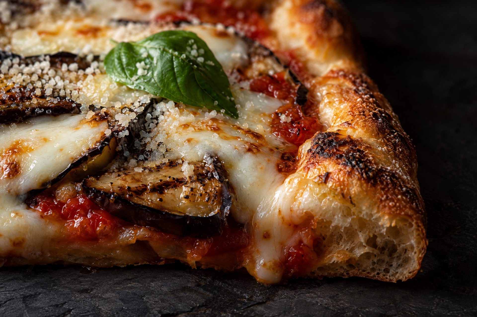 Closeup van pizza parmigiana: gesmolten mozzarella over goudbruine plakjes aubergine en een knapperige rand
