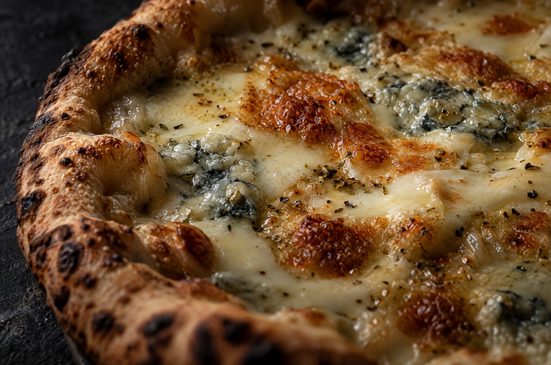 Close-up van gesmolten kaas op pizza quattro formaggi: romige gorgonzola tussen goudbruine plekken pecorino