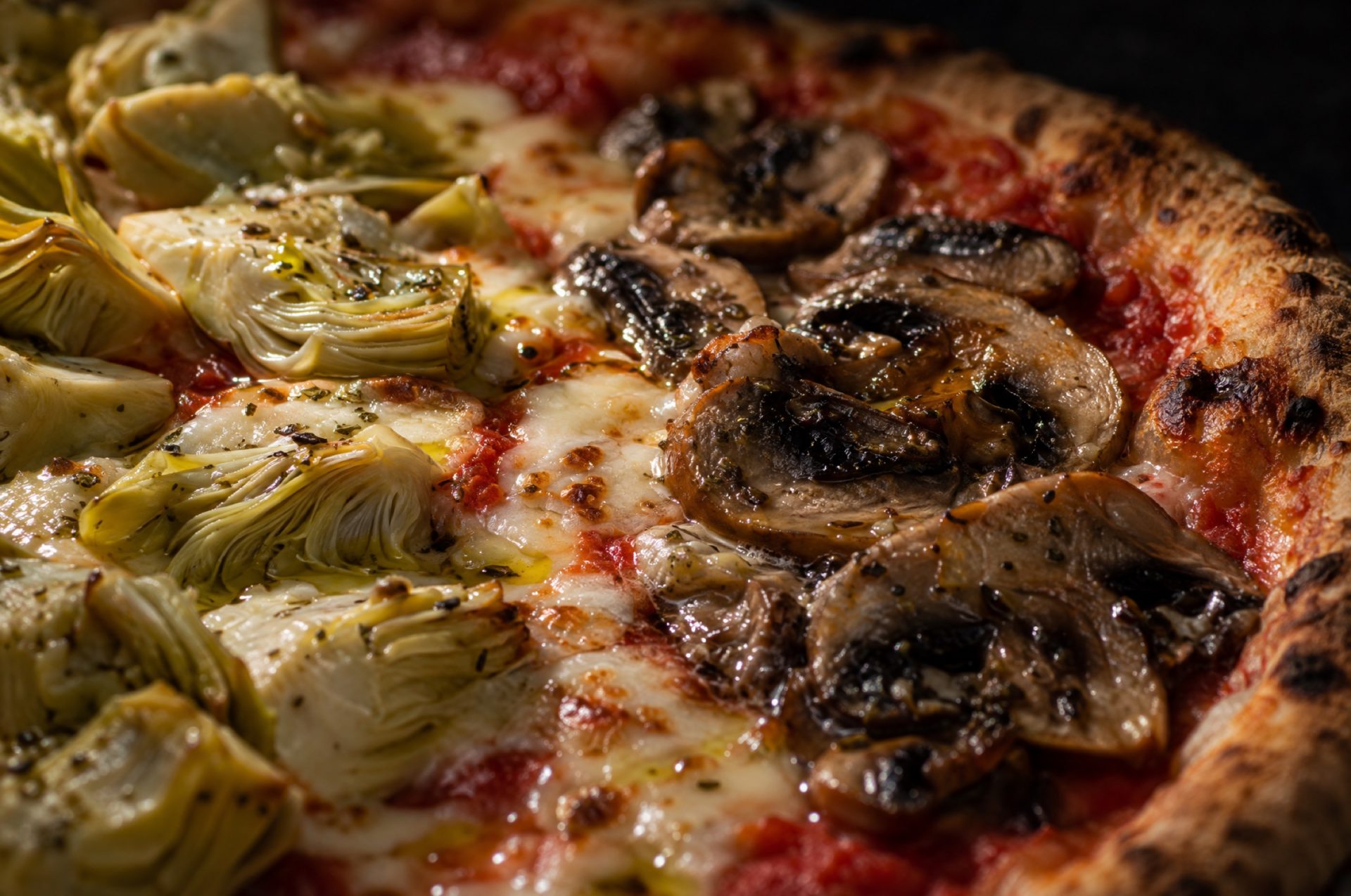 Close-up van pizza quattro stagioni waar de kwarten met artisjok en champignons elkaar raken, met gesmolten mozzarella