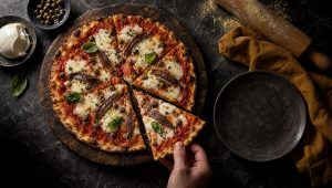Dunne pizza romana met tomaat, mozzarella, kappertjes en ansjovis op een donkere houten plank, met een deegroller ernaast
