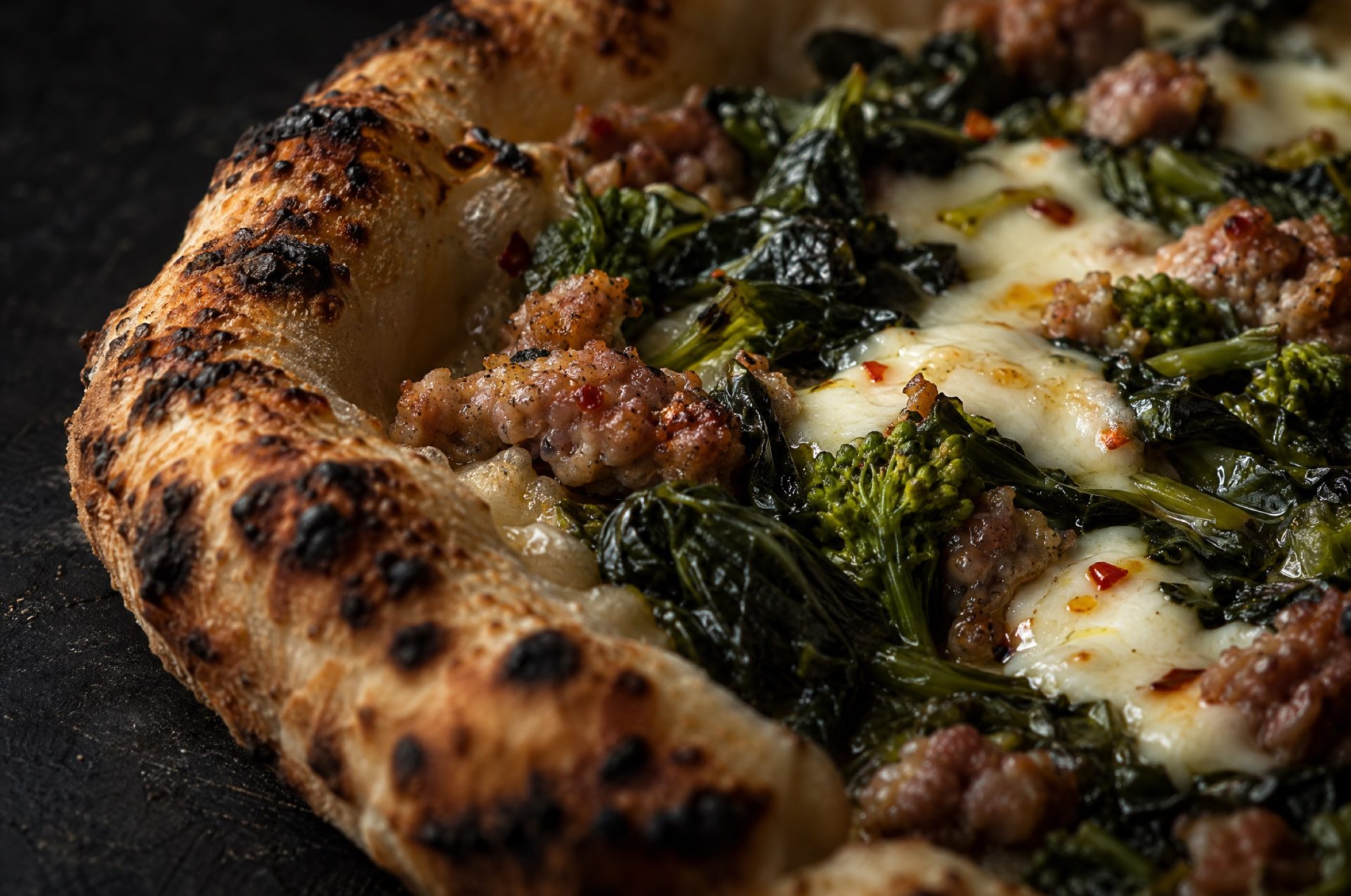 Close-up van pizza salsiccia met gesmoorde friarielli, kruimels salsiccia en gesmolten mozzarella op een luchtige rand