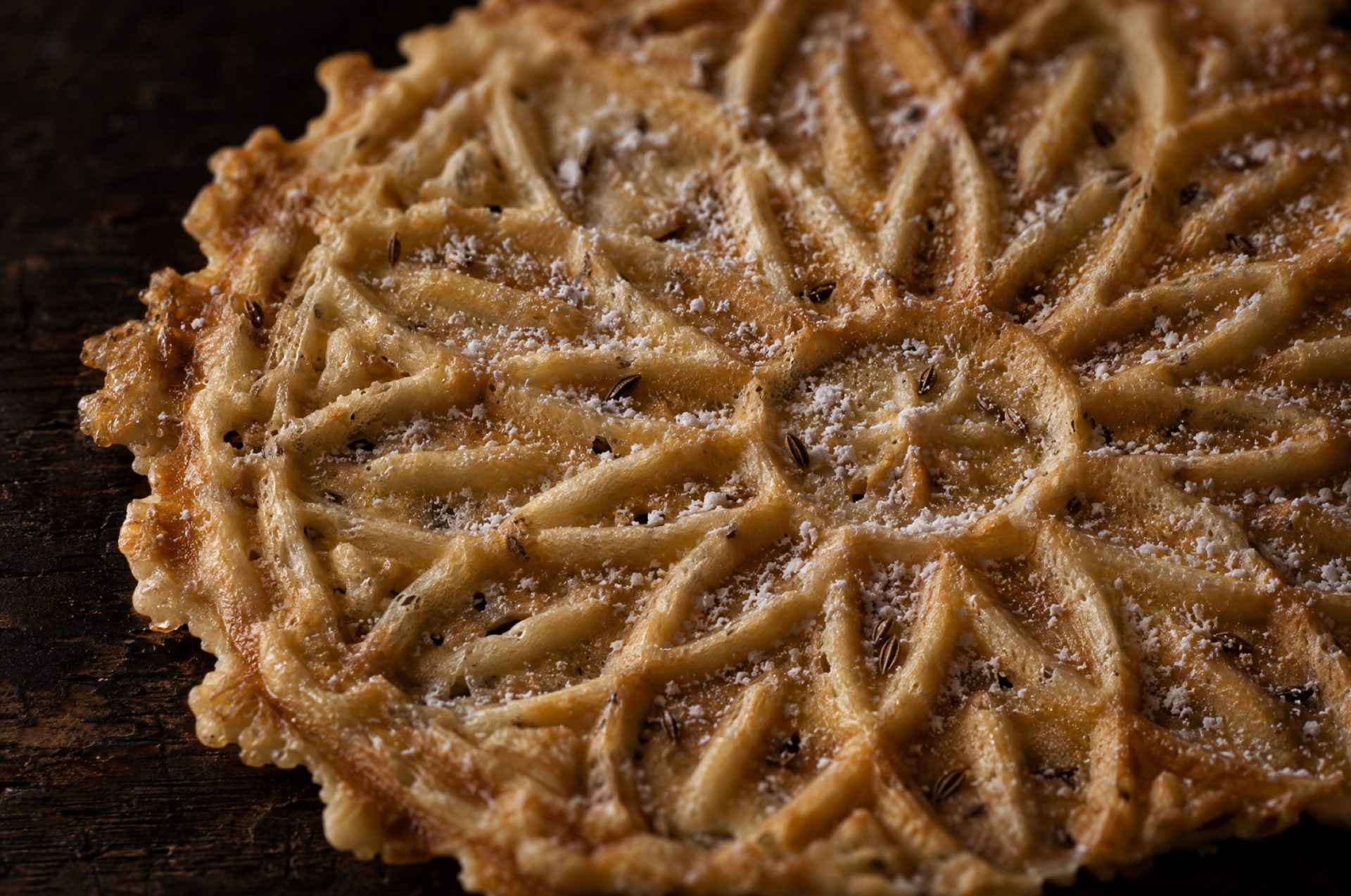 Close-up van pizzelle: het bloempatroon van het ijzer in het dunne, goudgele koekje met spikkels anijszaad
