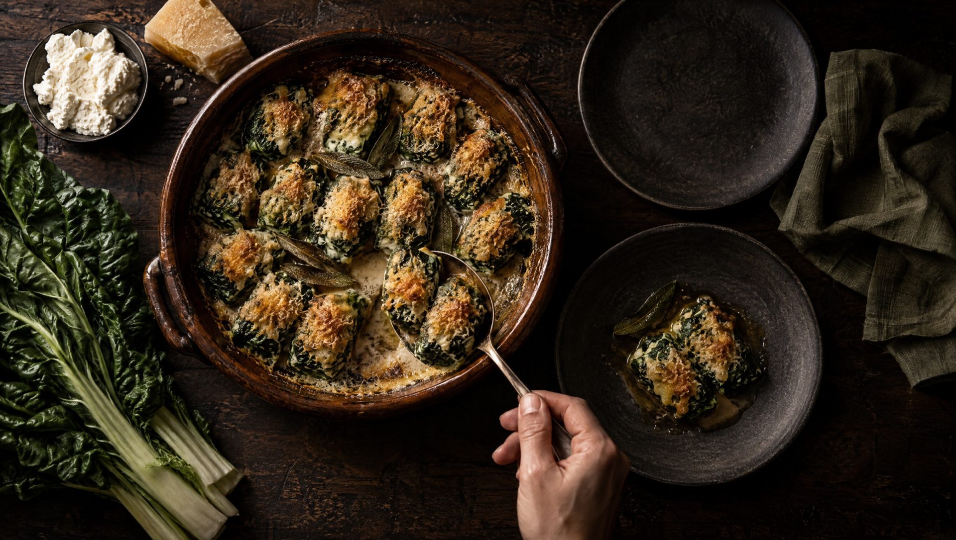 Ovenschaal rabaton met goudbruine Parmigiano en boter op een houten tafel in Piemonte, met snijbiet en ricotta ernaast