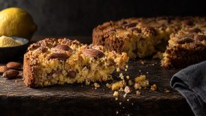 Gebroken stuk sbrisolona met amandelen met vel en losse kruimels op een donkere houten tafel, met maïsmeel en een citroen