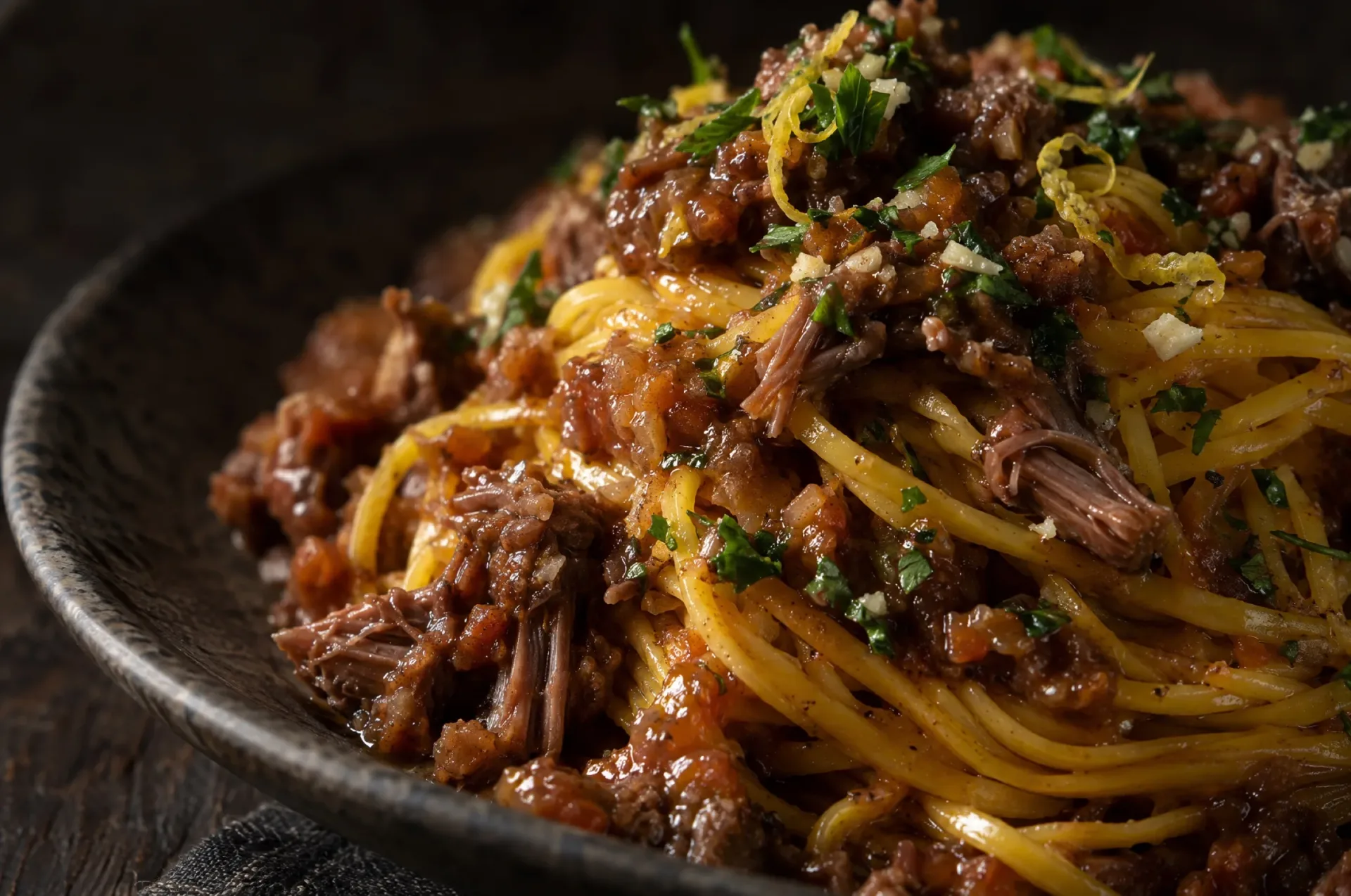 Close-up van tagliolini met ossobucoragù: gele draden met glanzende saus, plukjes kalfsvlees en groene snippers gremolata